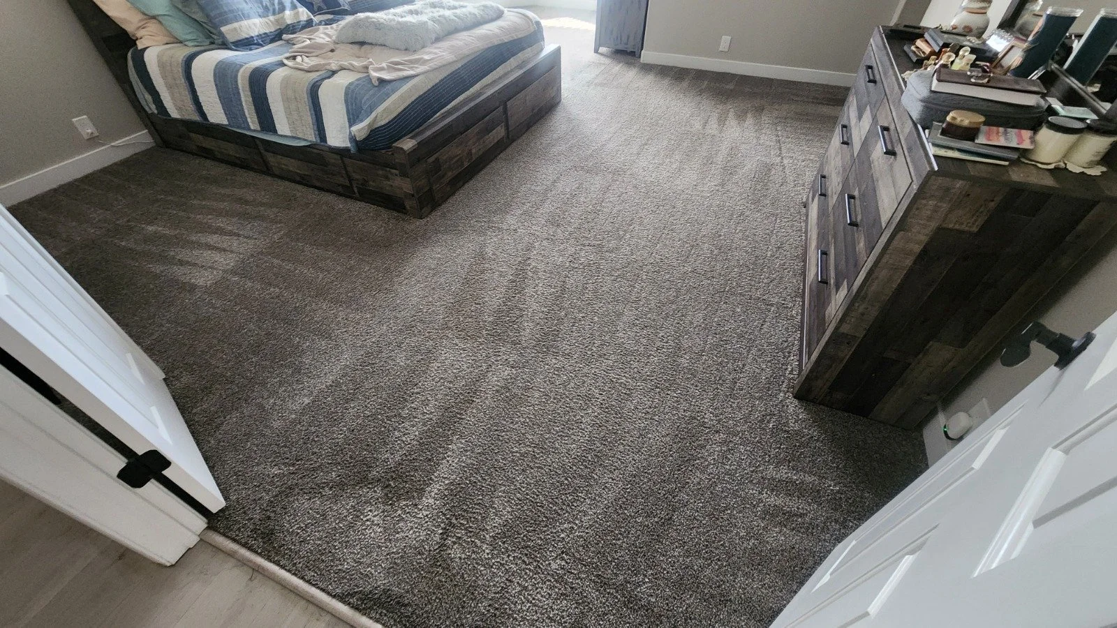 A bedroom with a bed at the top left corner, covered with a striped blue, white, and beige quilt. This carpet was professionally cleaned.