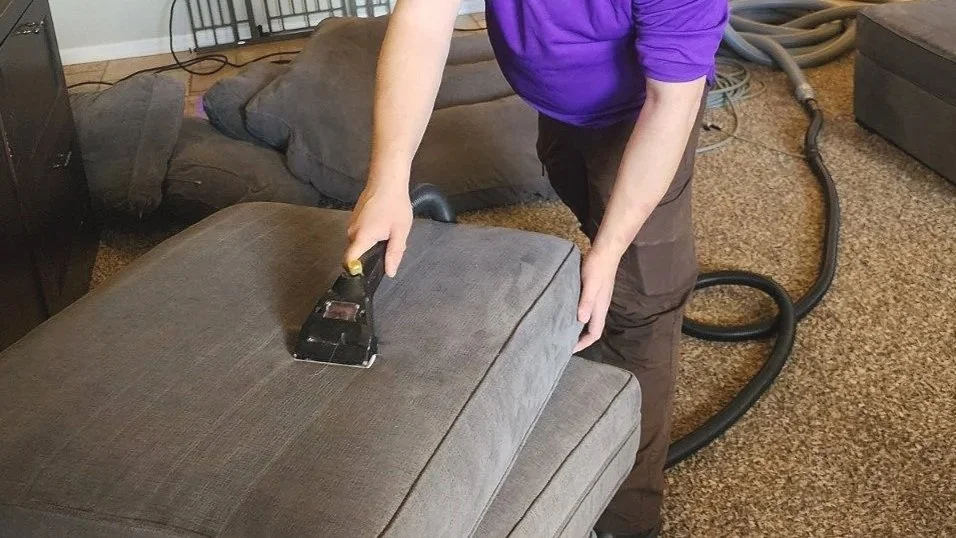 Person cleaning a sofa with a handheld steam cleaner.