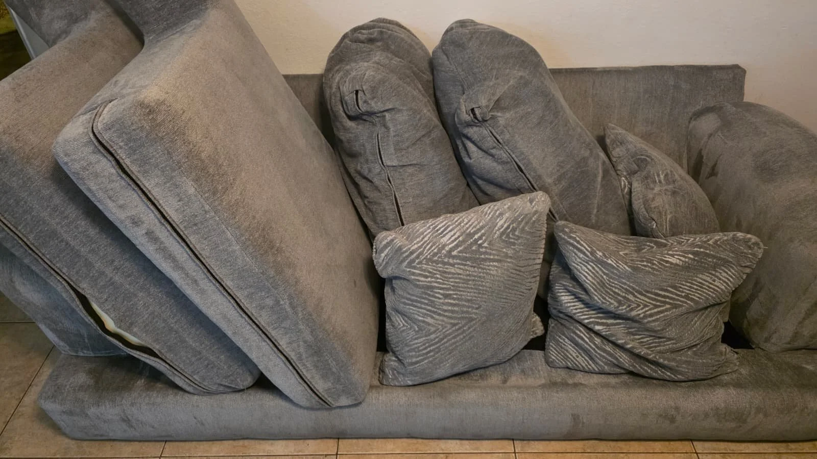 A grey fabric sofa with five cushions, four with a striped pattern and one plain, arranged on and around the sofa.