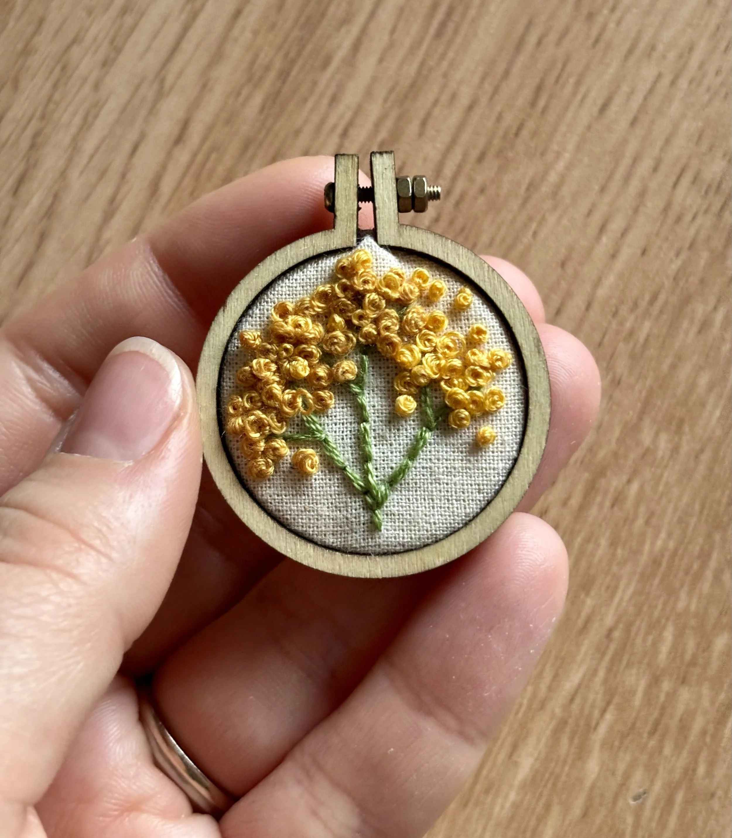 A small embroidery hoop with a fabric background featuring a yellow floral embroidery design.