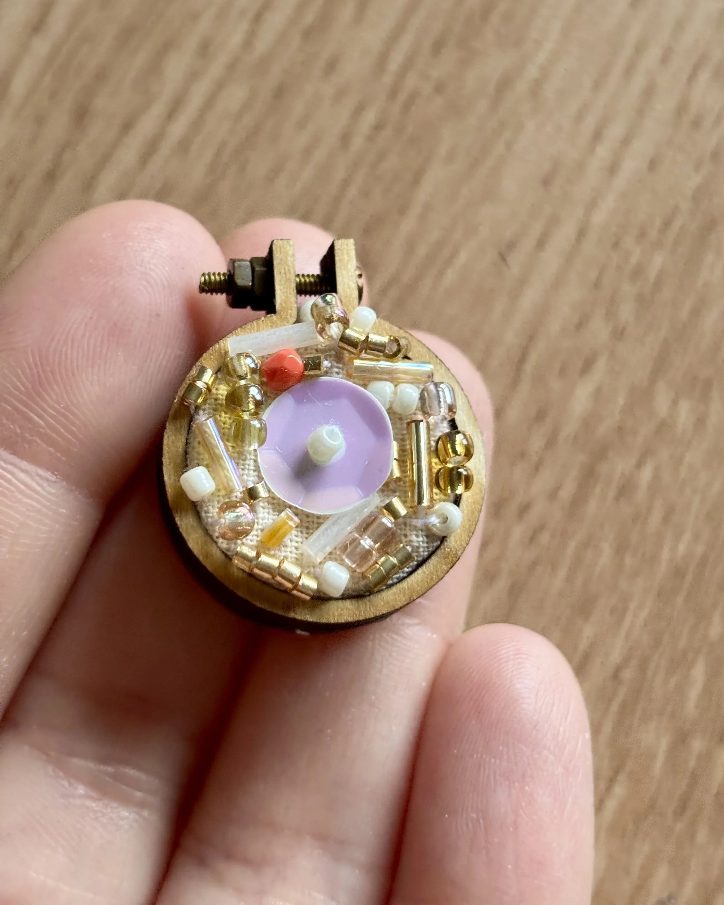 Miniature wooden spinning top decorated with various tiny beads and rhinestones, resting on a person's fingers.