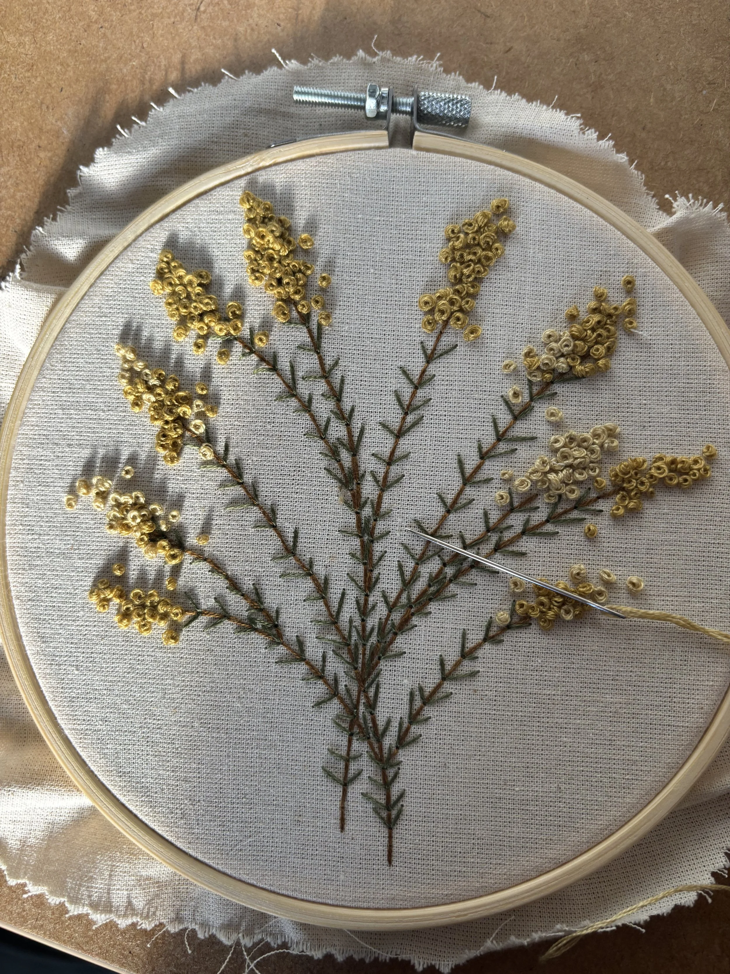 Embroidery hoop with a fabric and a sprig of yellow flowers stitched onto it.