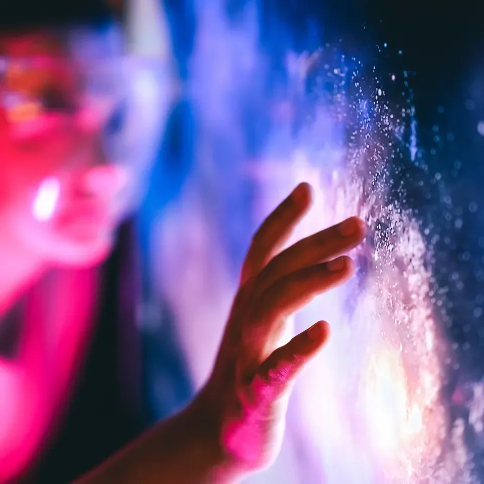 Person touching a colorful, starry, and nebulous digital display with their hand, with a blurry face in the background.