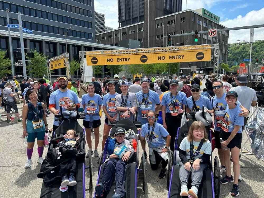 Group of people, including children and adults, gathered in front of a 'No Entry' barricade at a race event in an urban area with tall buildings.
