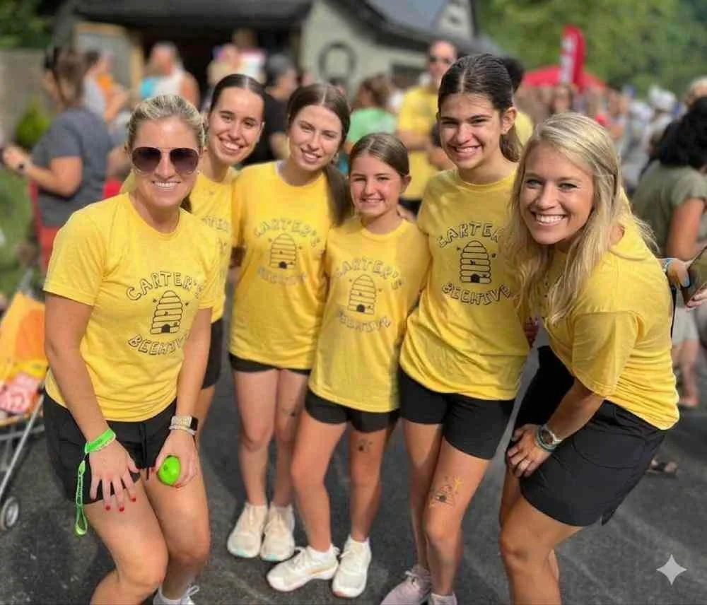 Group of six young women wearing yellow t-shirts with beehive graphic and text, smiling at an outdoor event.