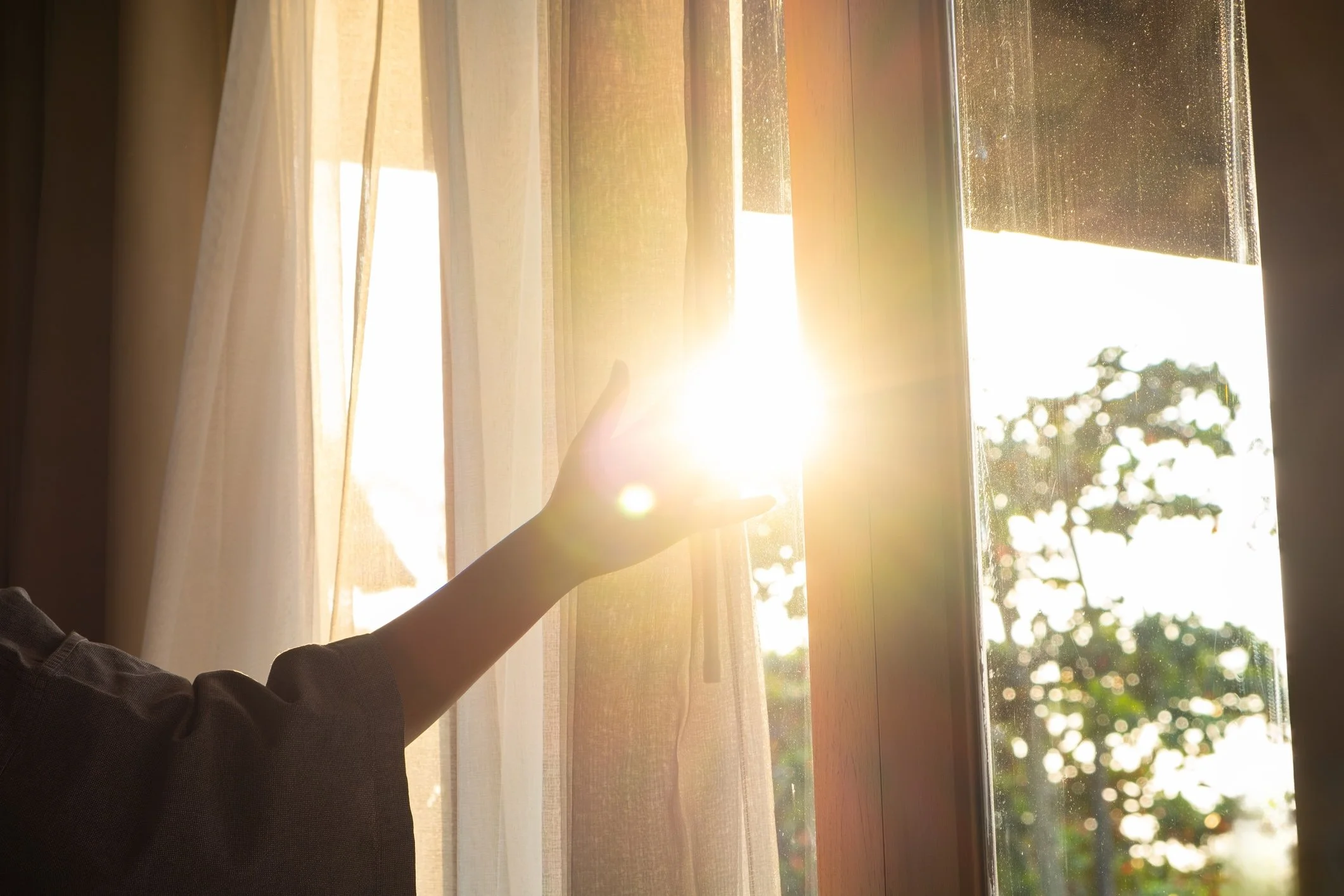 Woman reaching out hand to sunlight coming through window