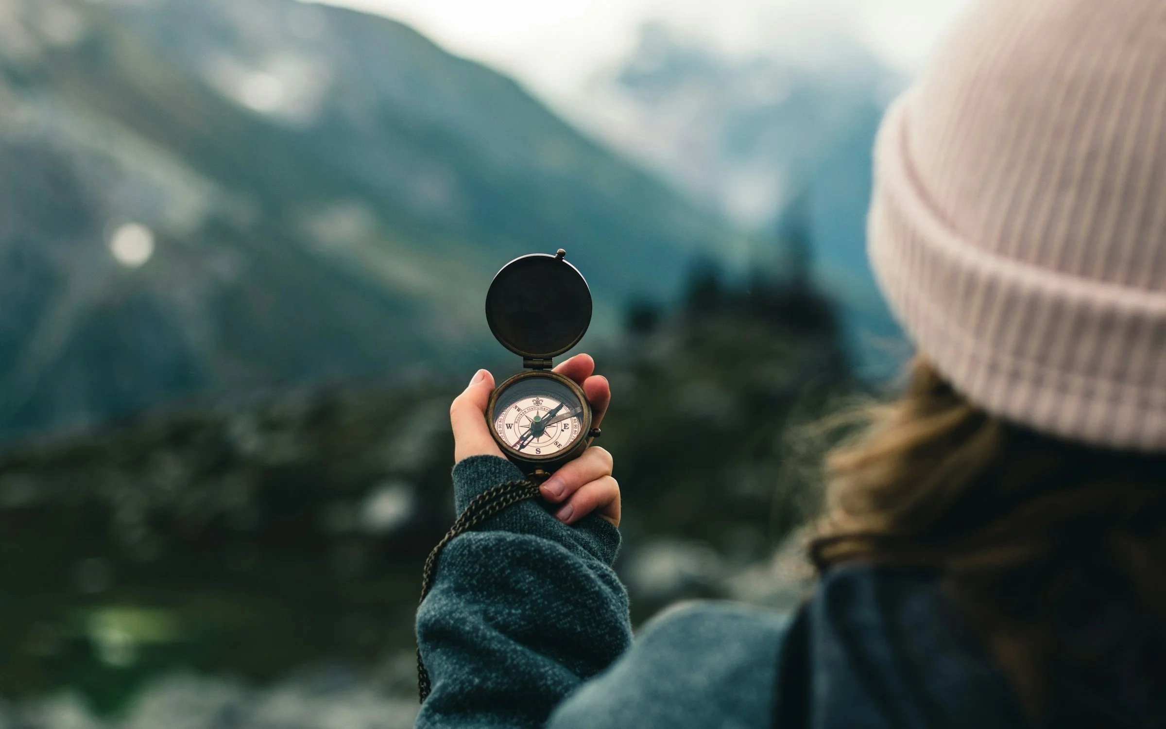 Person holding a compass with a mountainous landscape in the background.