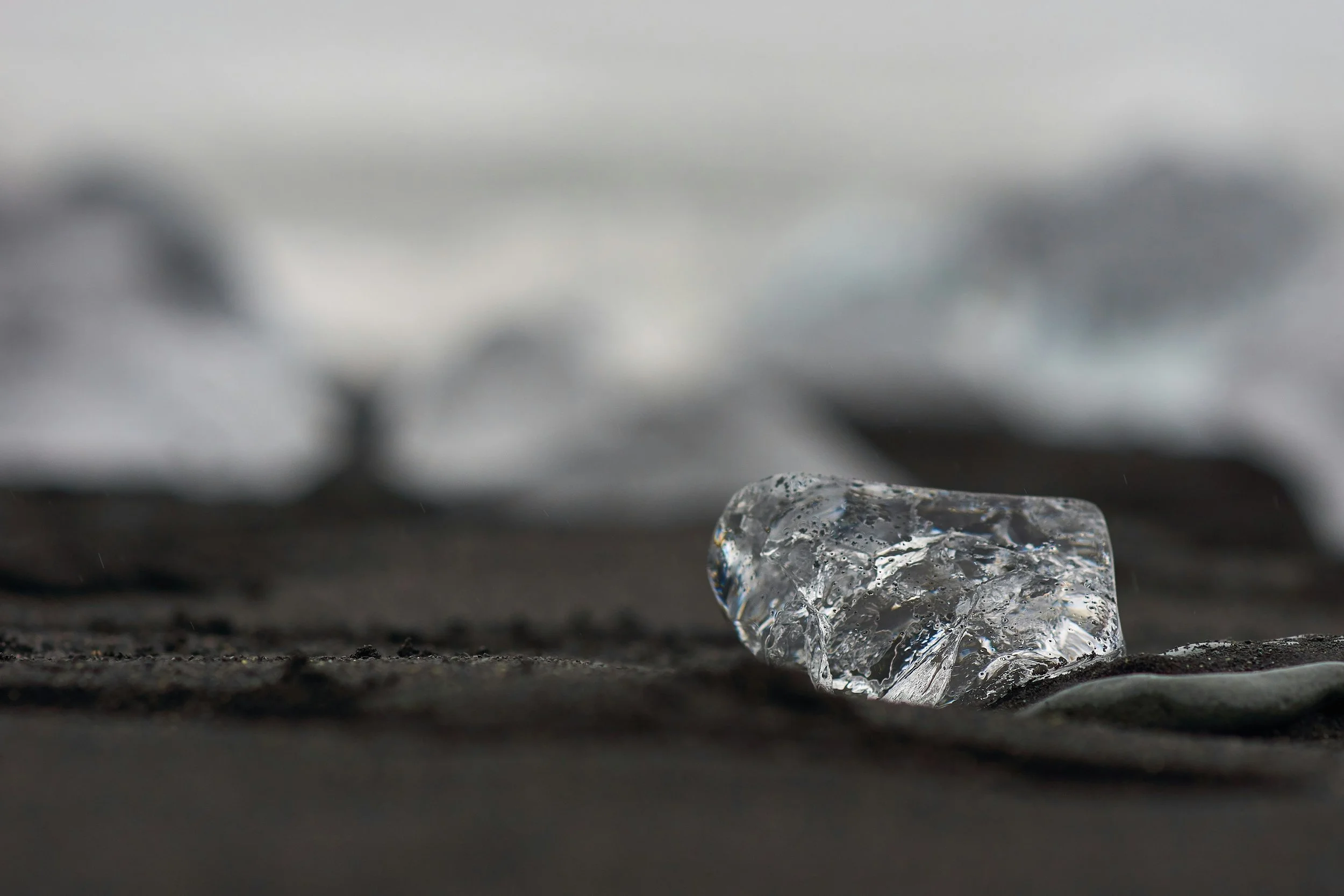 Close-up of a partially melted ice cube on a dark surface with blurred background.