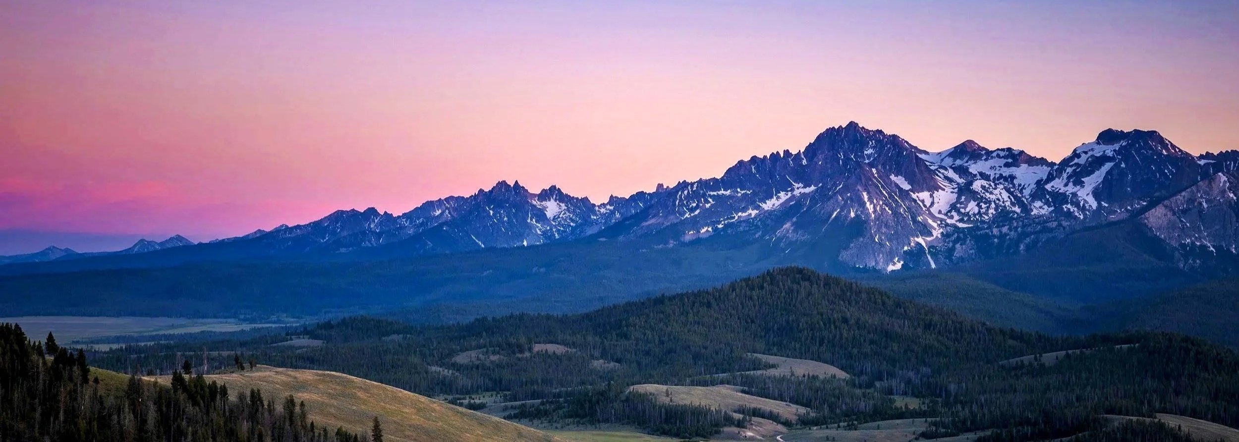 Snow-capped mountains at sunset with a pink and purple sky.
