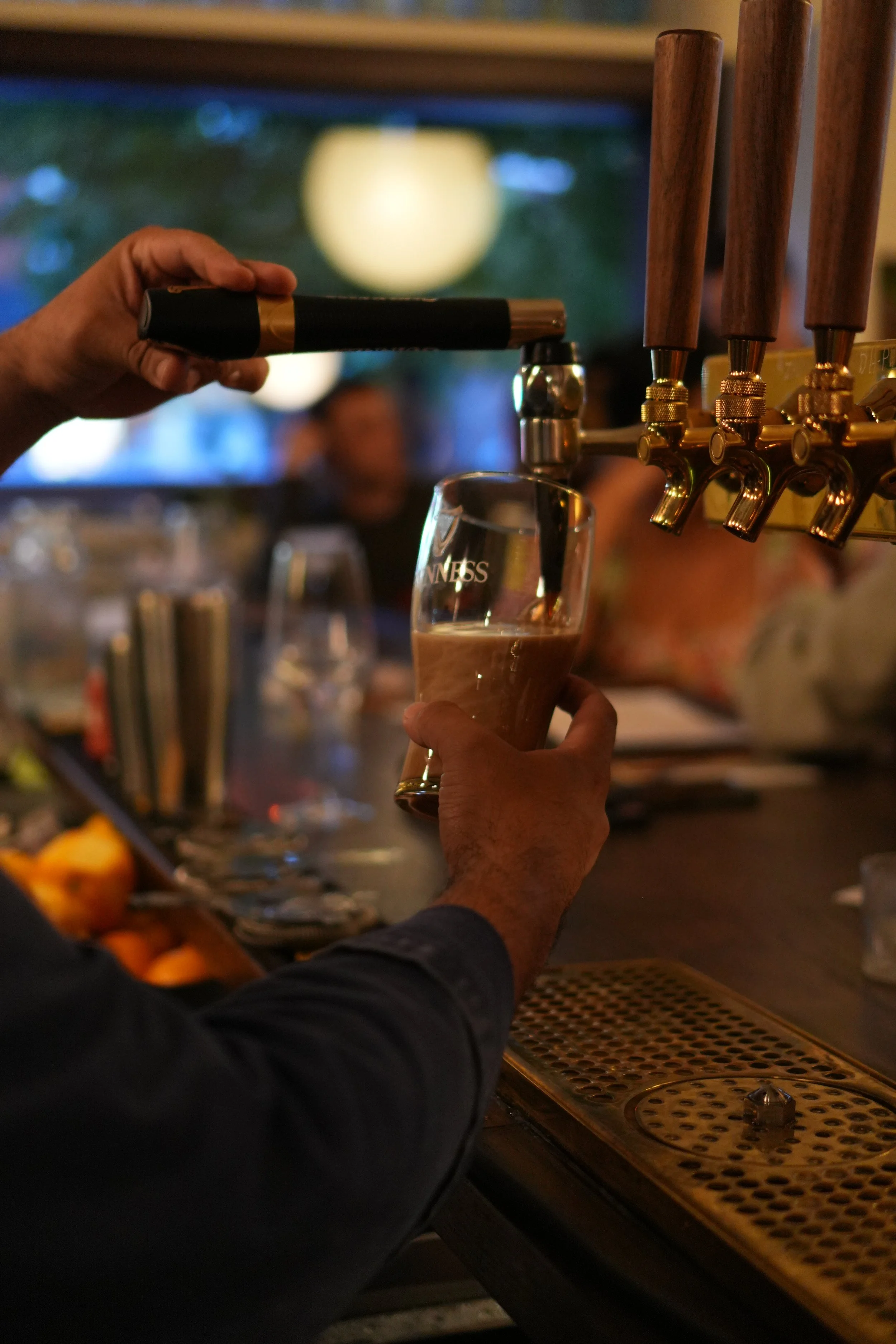 A person is pouring beer from a tap into a glass at Bar Alice Anne, with the Guinness logo visible on the glass and the bar's beer taps in the background.