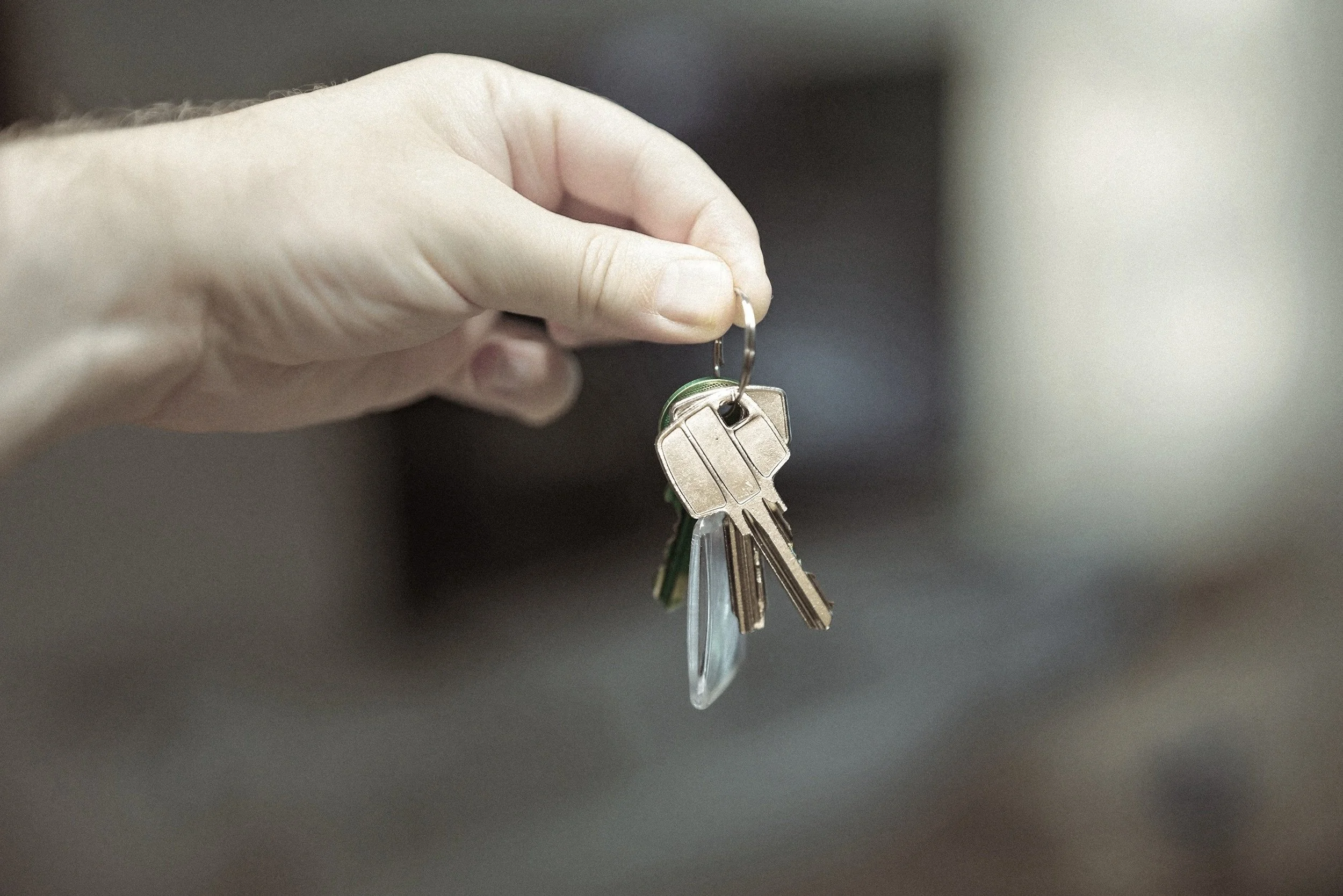 A hand holding a keyring with multiple keys, with a blurred background.