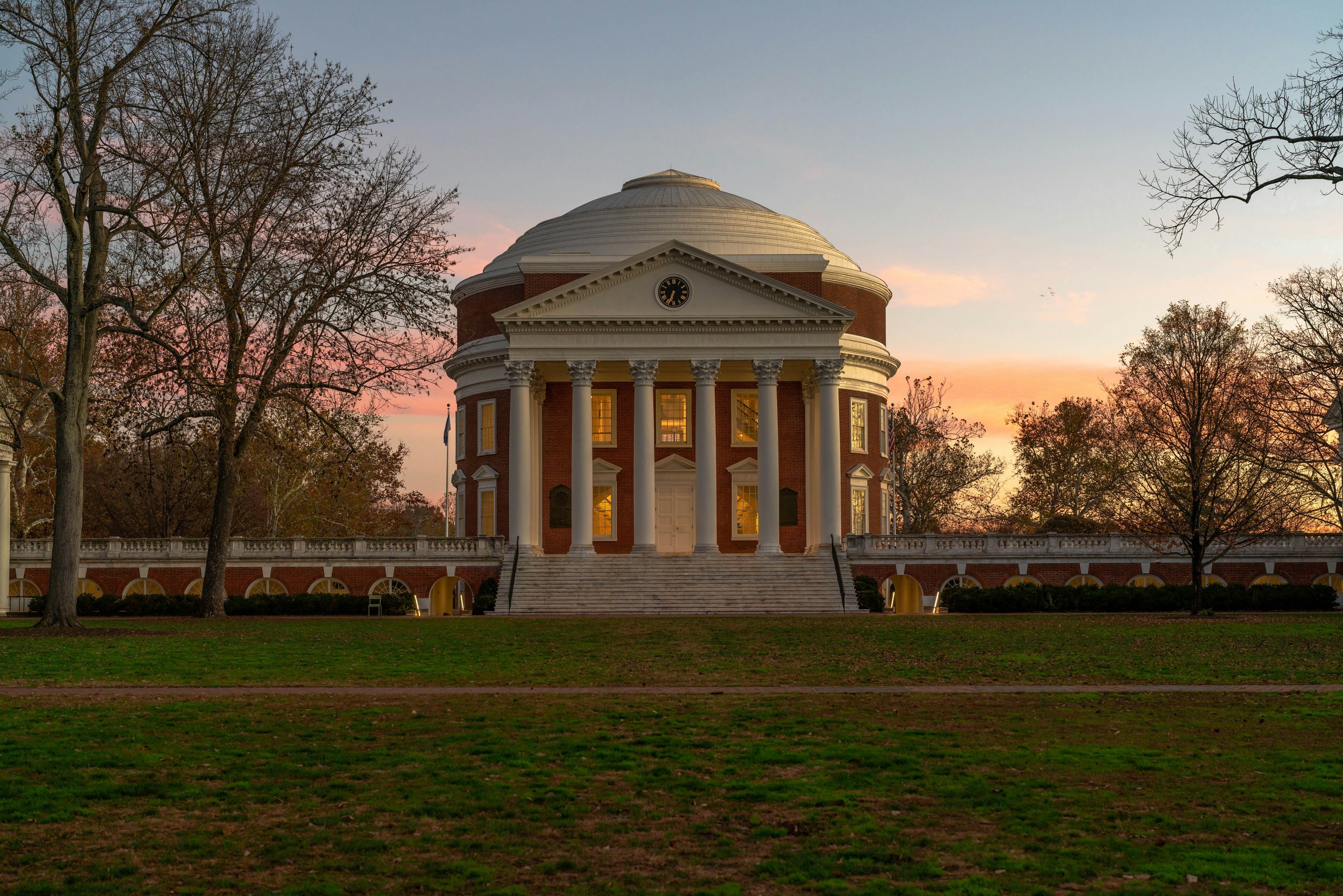 The Jefferson Memorial with a circular dome, classical columns, and stairs leading up to the entrance, surrounded by trees during sunset.