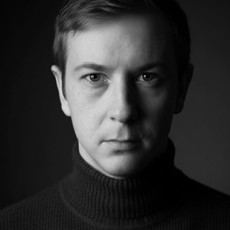 Musta-valkoinen valokuva miesni kasvot läheltä, istuu ristikotakki päällä, katsoo suoraan kameraan