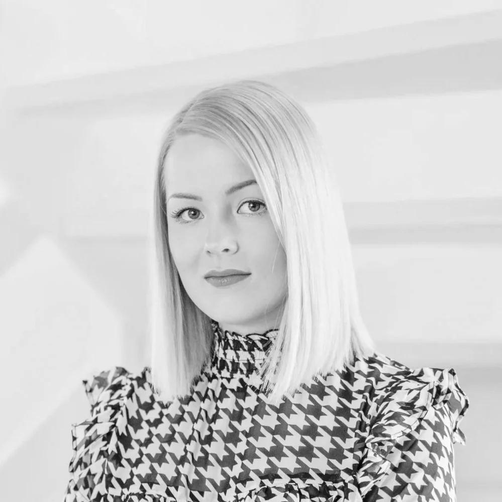 Mustavalkovalokuva naisesta, jolla on suorat, vaaleat hiukset ja rusetin kaltainen pusero.