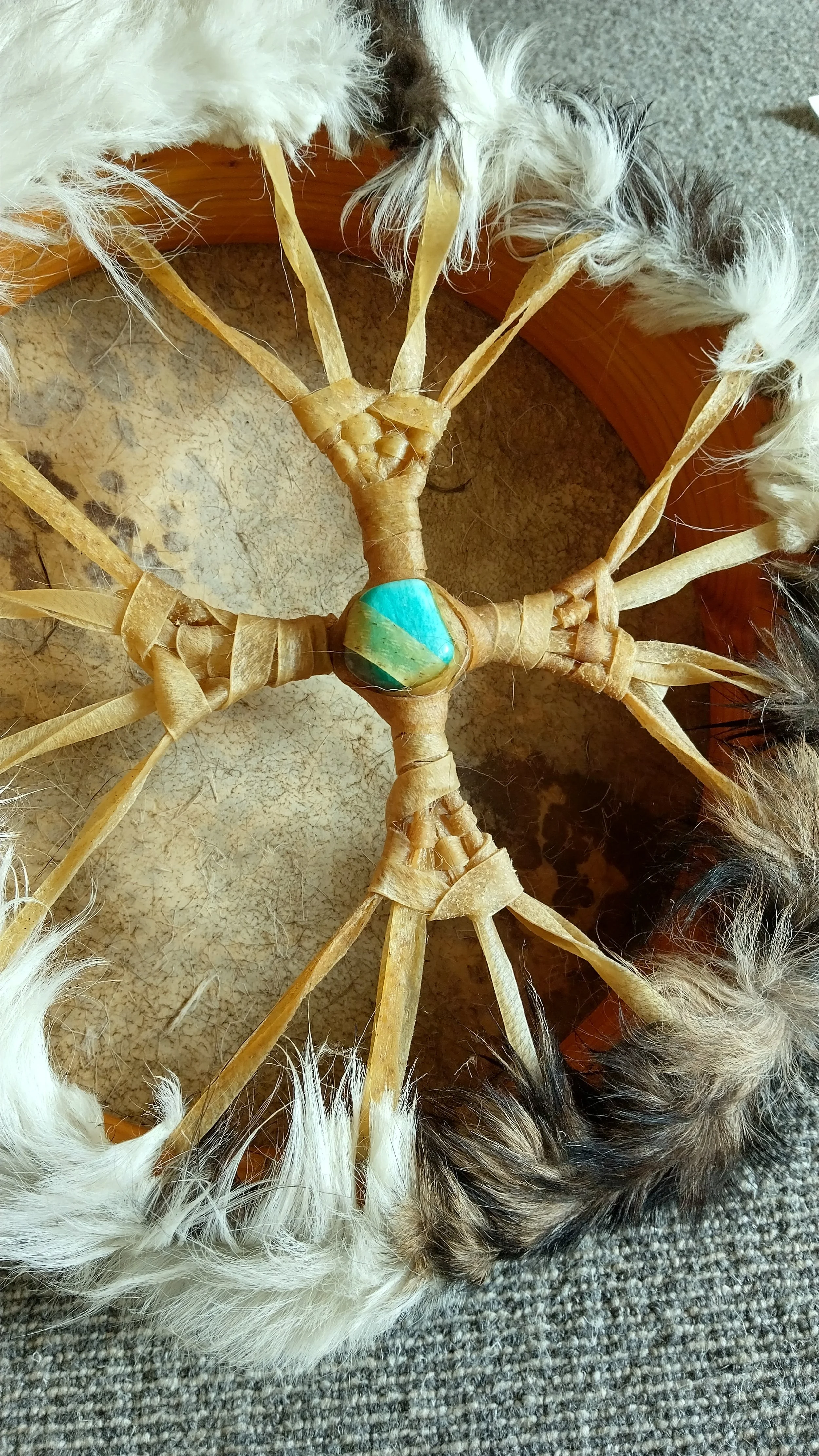 A dreamcatcher with a central bead, wrapped with leather strips, featuring feathers around its circle, placed on a textured surface.