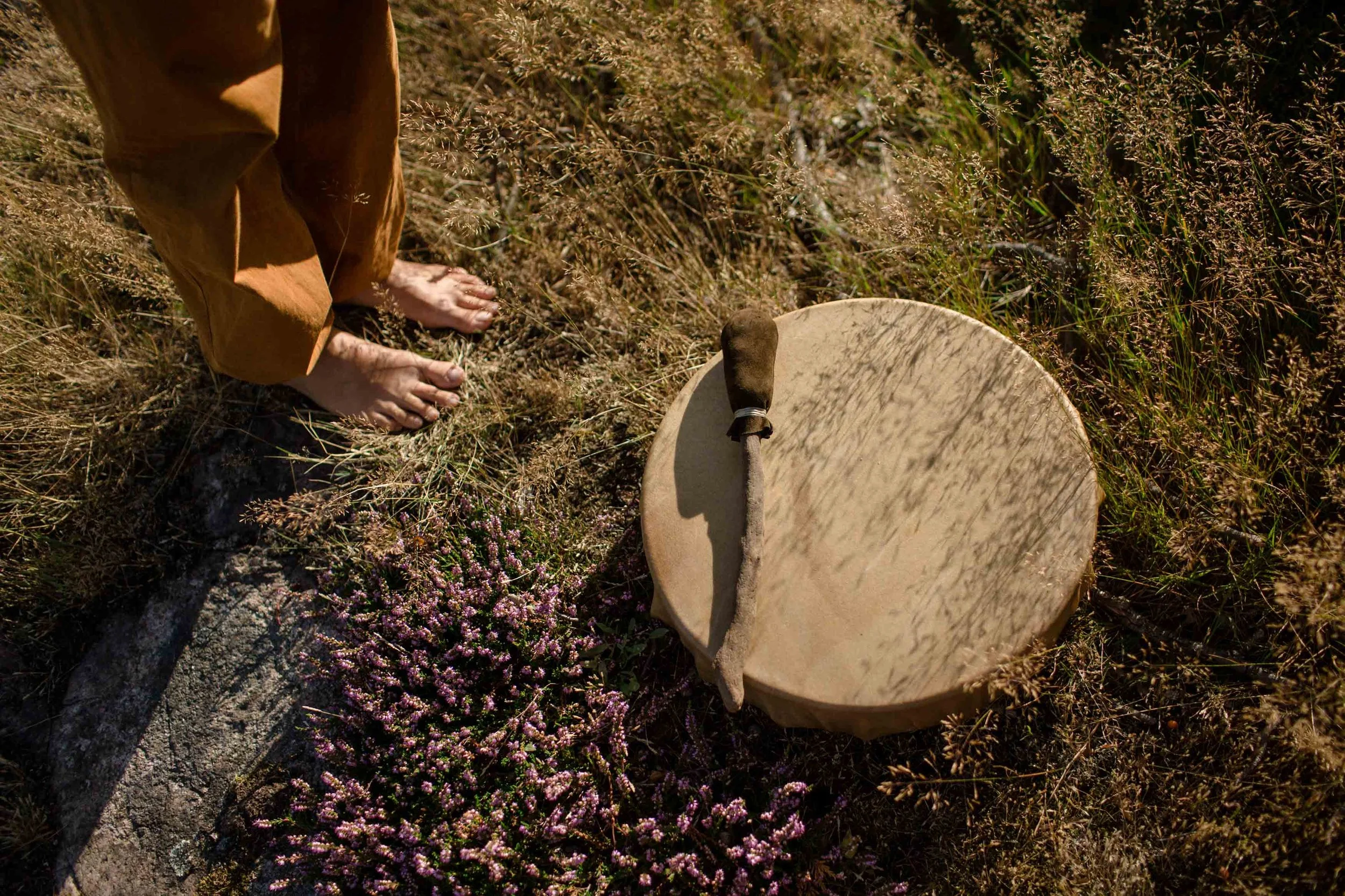 Bare feet are standing on summergrass and heather, with a shamanic drum lying beside