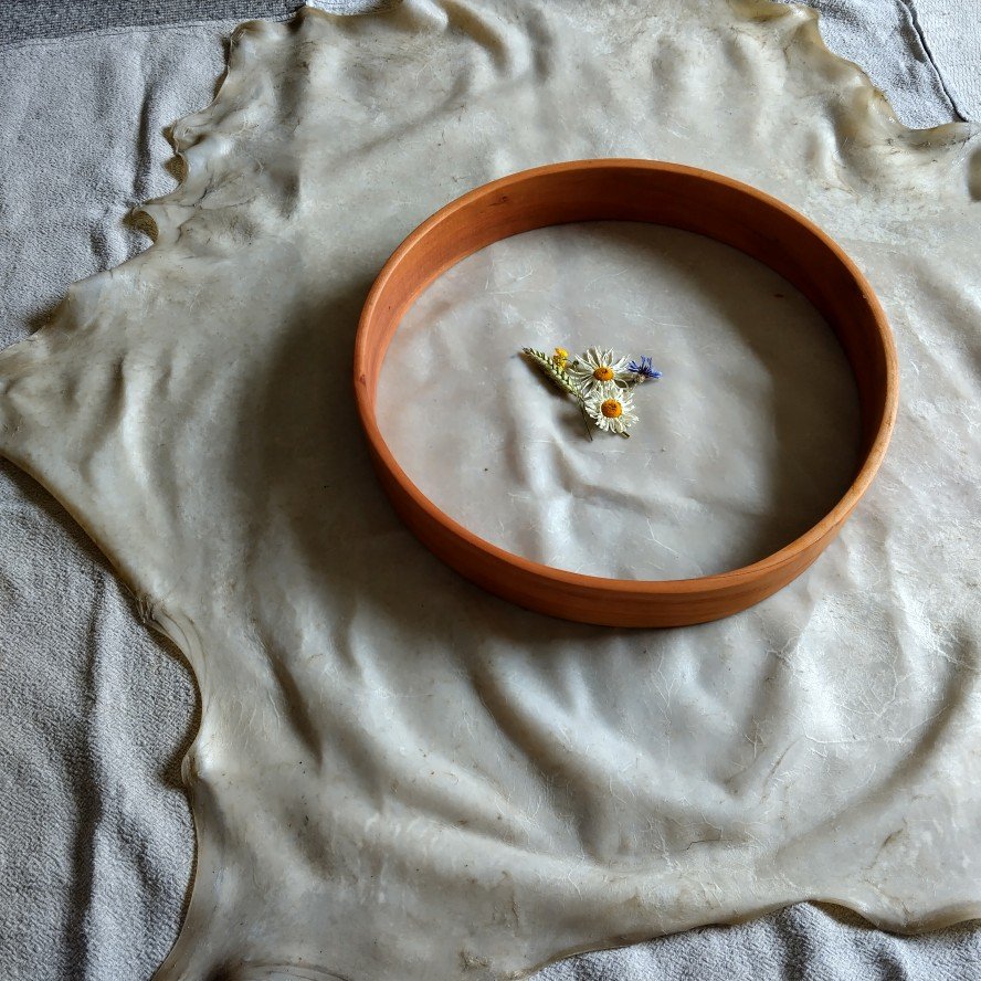 A leather hide with a round wooden or terracotta ring on it, containing small dried wildflowers in the center.
