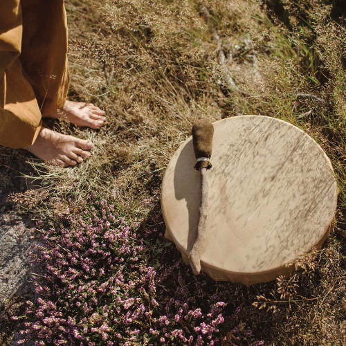 Bare feet are standing on summergrass and heather, with a shamanic drum lying beside