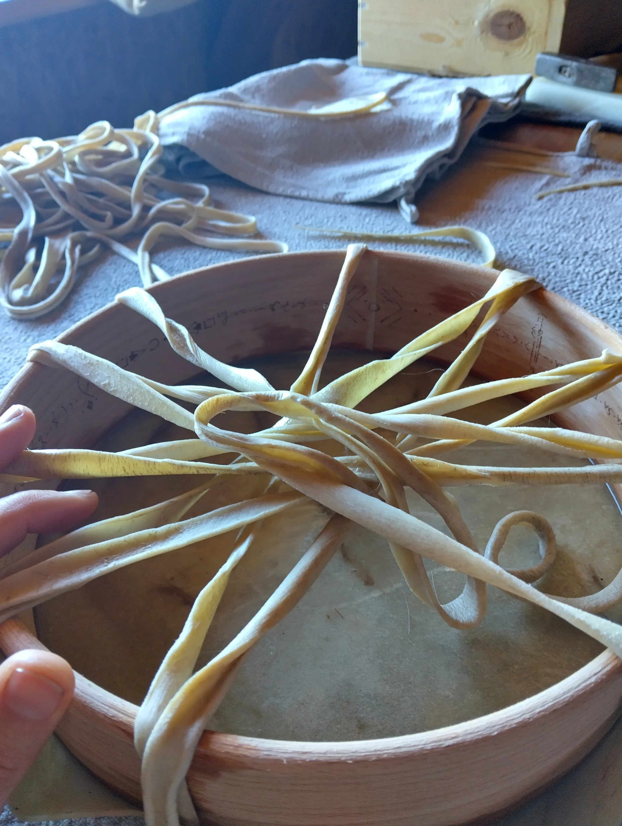 Unwooden tray filled with freshly made homemade pasta noodles, with additional noodles and kitchen items in the background.