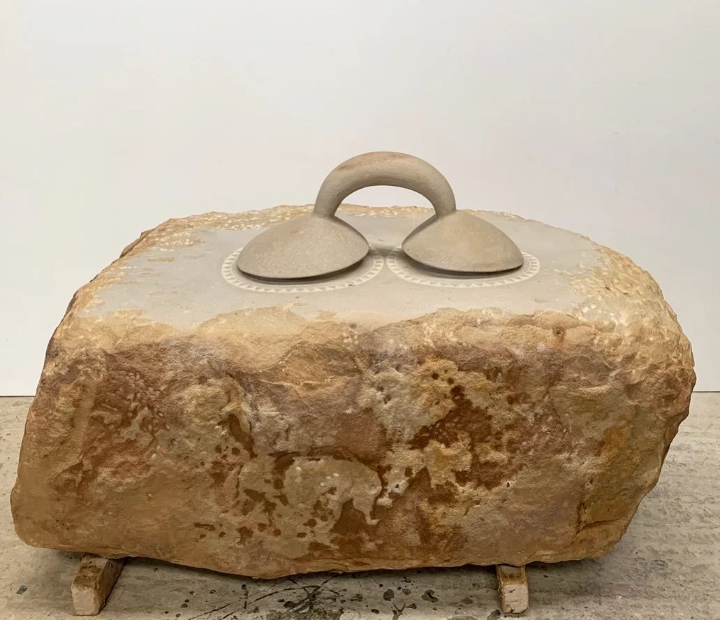 A stone sculpture with two circular shapes connected by an arch on top of a large, rough stone base.