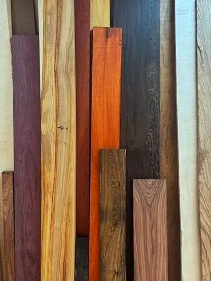 Various wooden planks in different colors and grain patterns leaning against a wall.