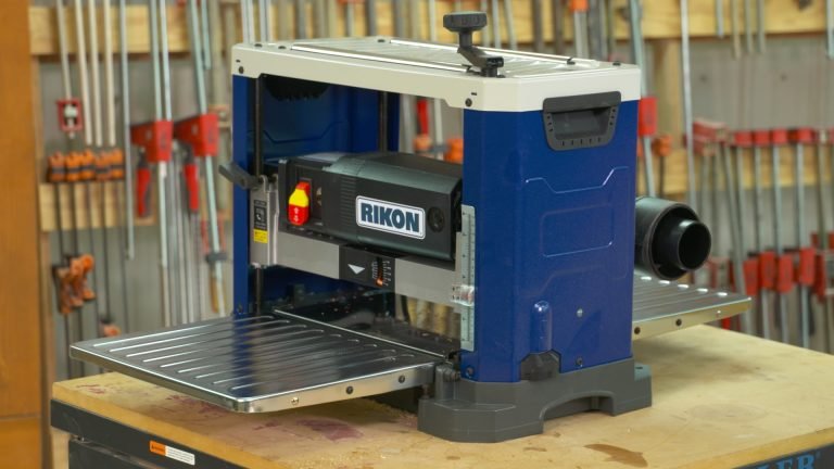 A compact benchtop RIKON woodworking planer situated on a wooden workbench in a workshop.