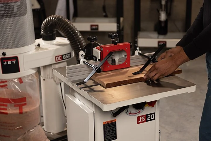 A JET router with a wooden workpiece, clamps, and a person's hands guiding it.