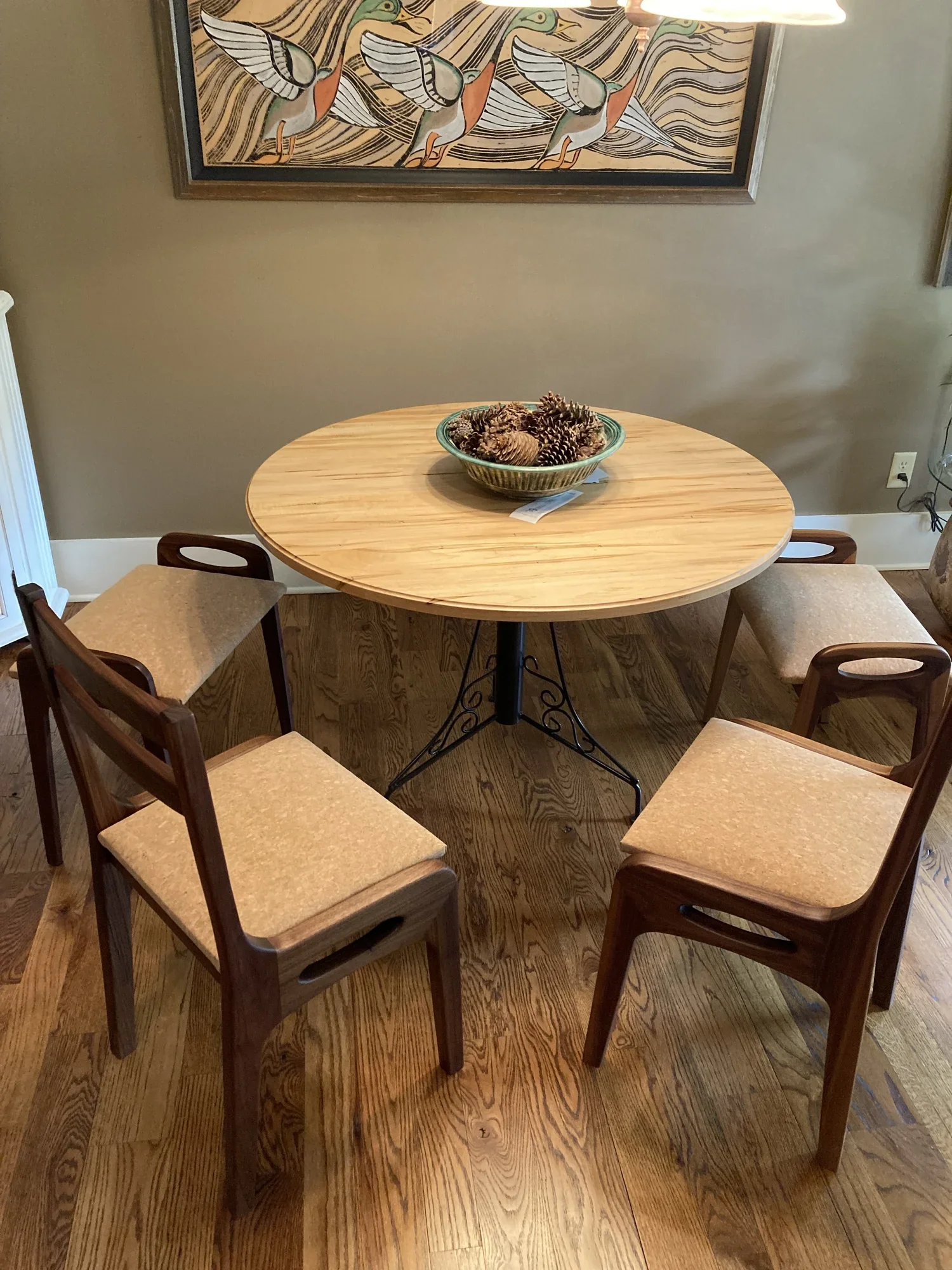 Wooden dining table with four chairs and a bowl of pinecones on top, in a room with a wall artwork of birds.