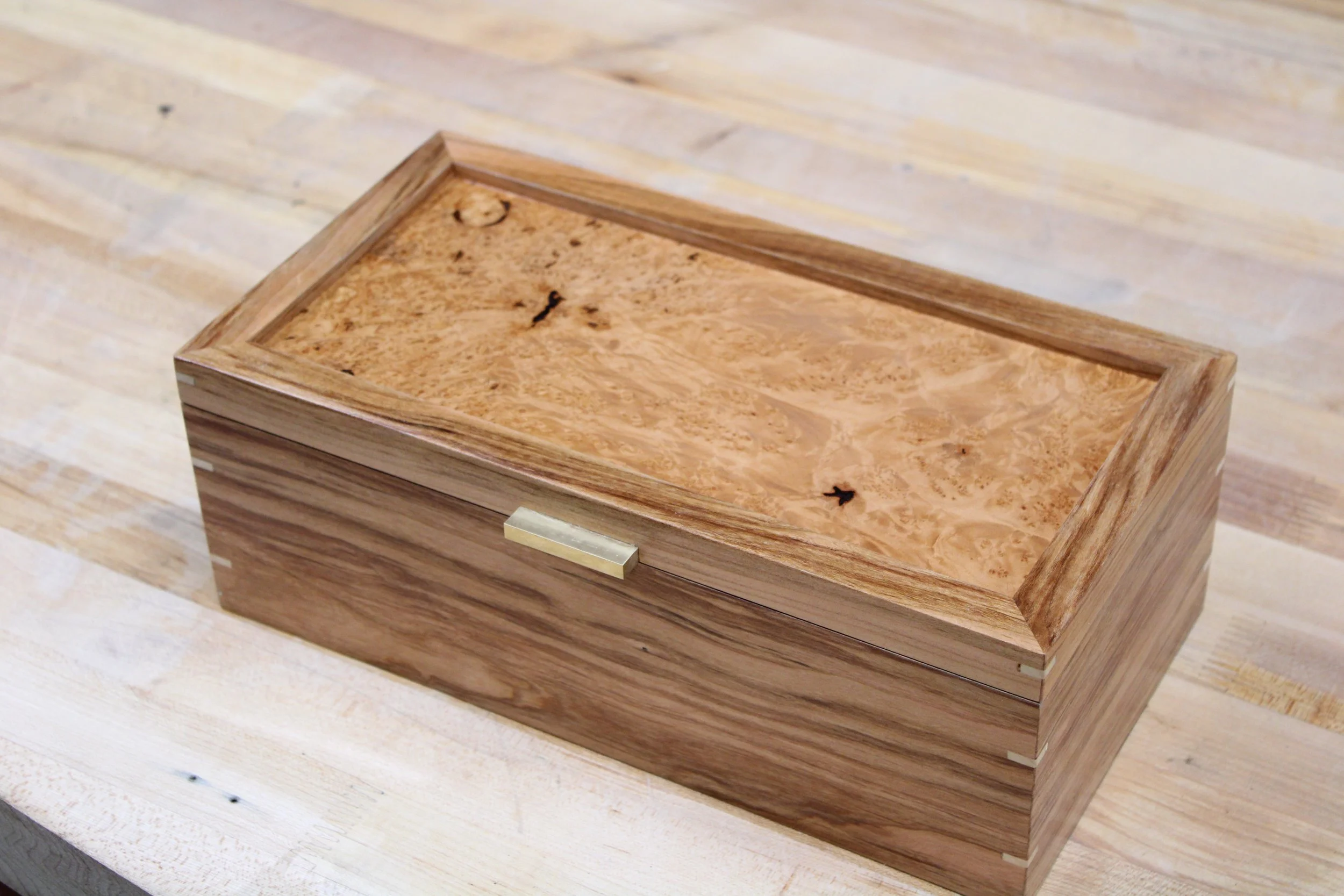 A wooden box with a natural wood finish, placed on a light-colored wooden surface, built by a woodworker at The Woodwork Shop. 
