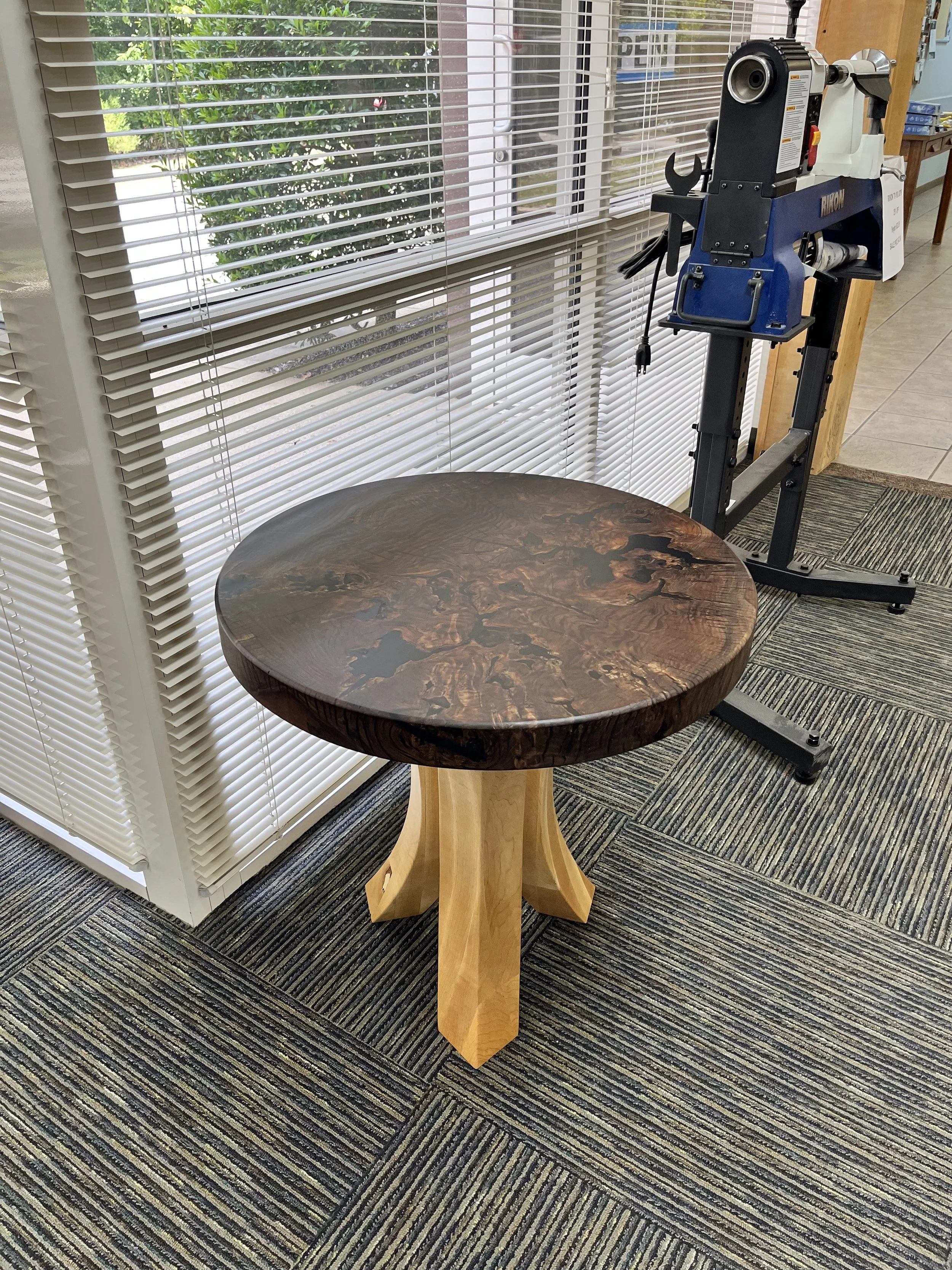 A round wooden table with a polished dark wood top and light wooden legs built by a woodworker at The Woodwork Shop.