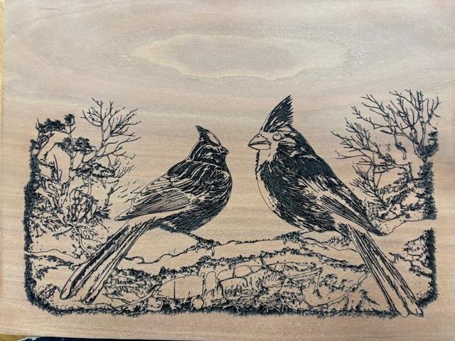 Line drawing of two birds perched on a branch, with trees on either side, made with a laser engraver at The Woodwork Shop. 