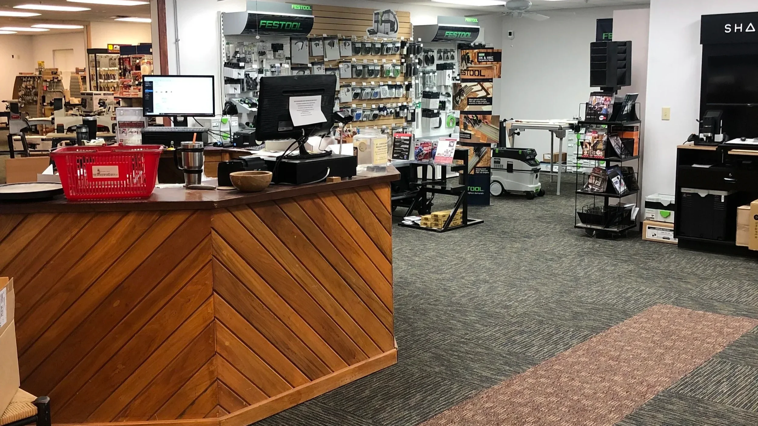 Interior of The Woodwork Shop with a handmade wooden counter, computer, cash register, and various tools and supplies on shelves in the background, including Festool, Sawstop and Shaper Origin.