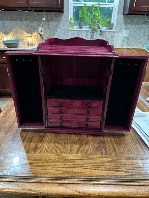 A partially opened wooden jewelry box with drawers inside.