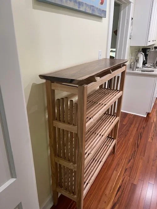 Wooden shoe rack with four slatted shelves in a kitchen area.