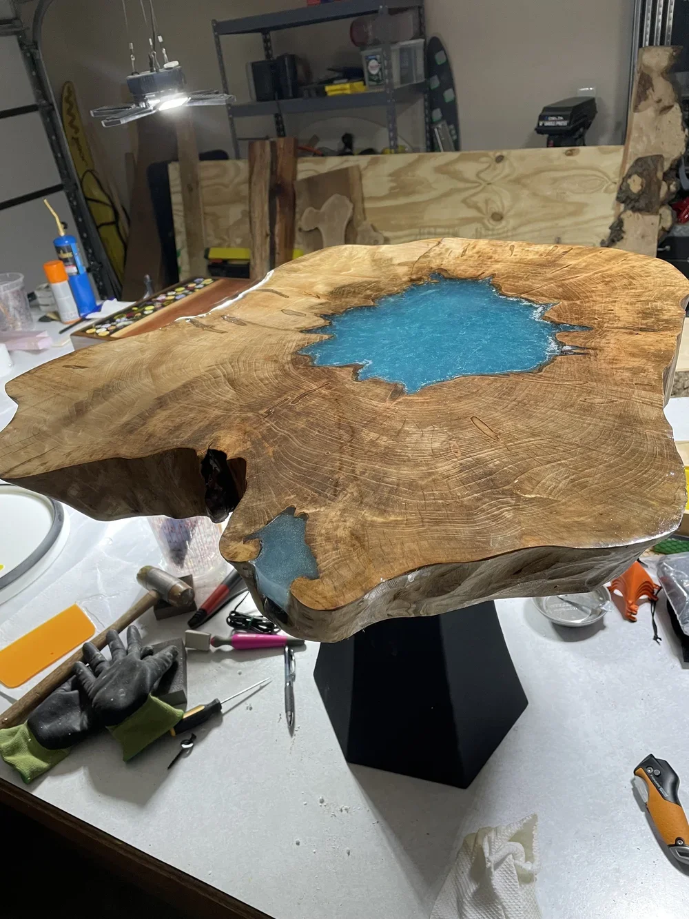A woodworking project featuring a large, polished wood slab with a resin-filled center in a workshop workspace.