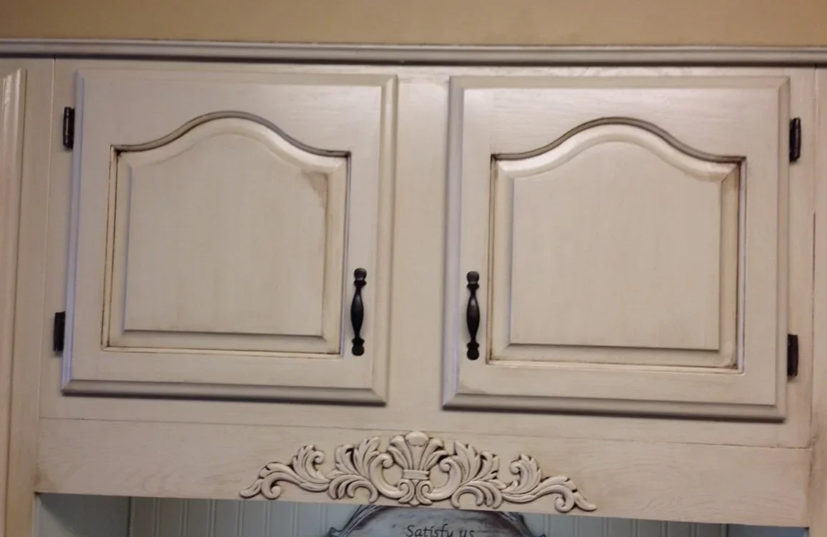 White kitchen cabinet doors with black handles and decorative carving below.