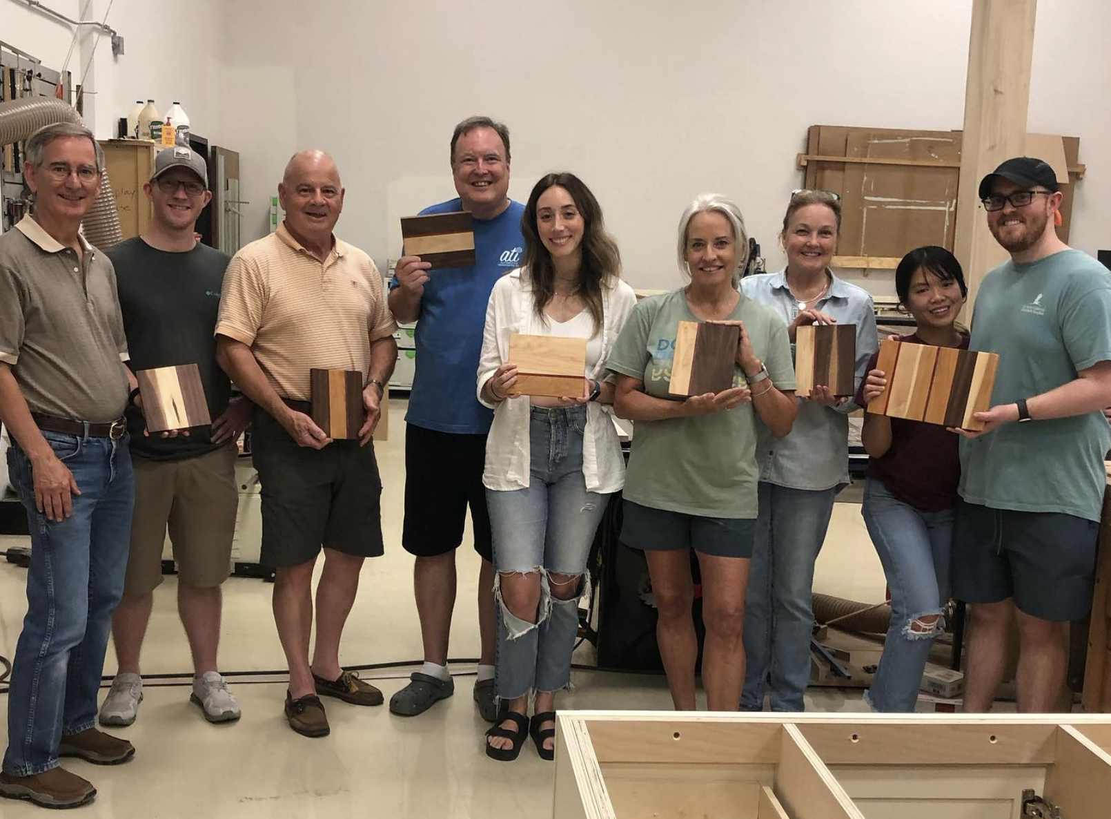 Group of ten people standing in The Woodwork Shop each holding a small wooden box.