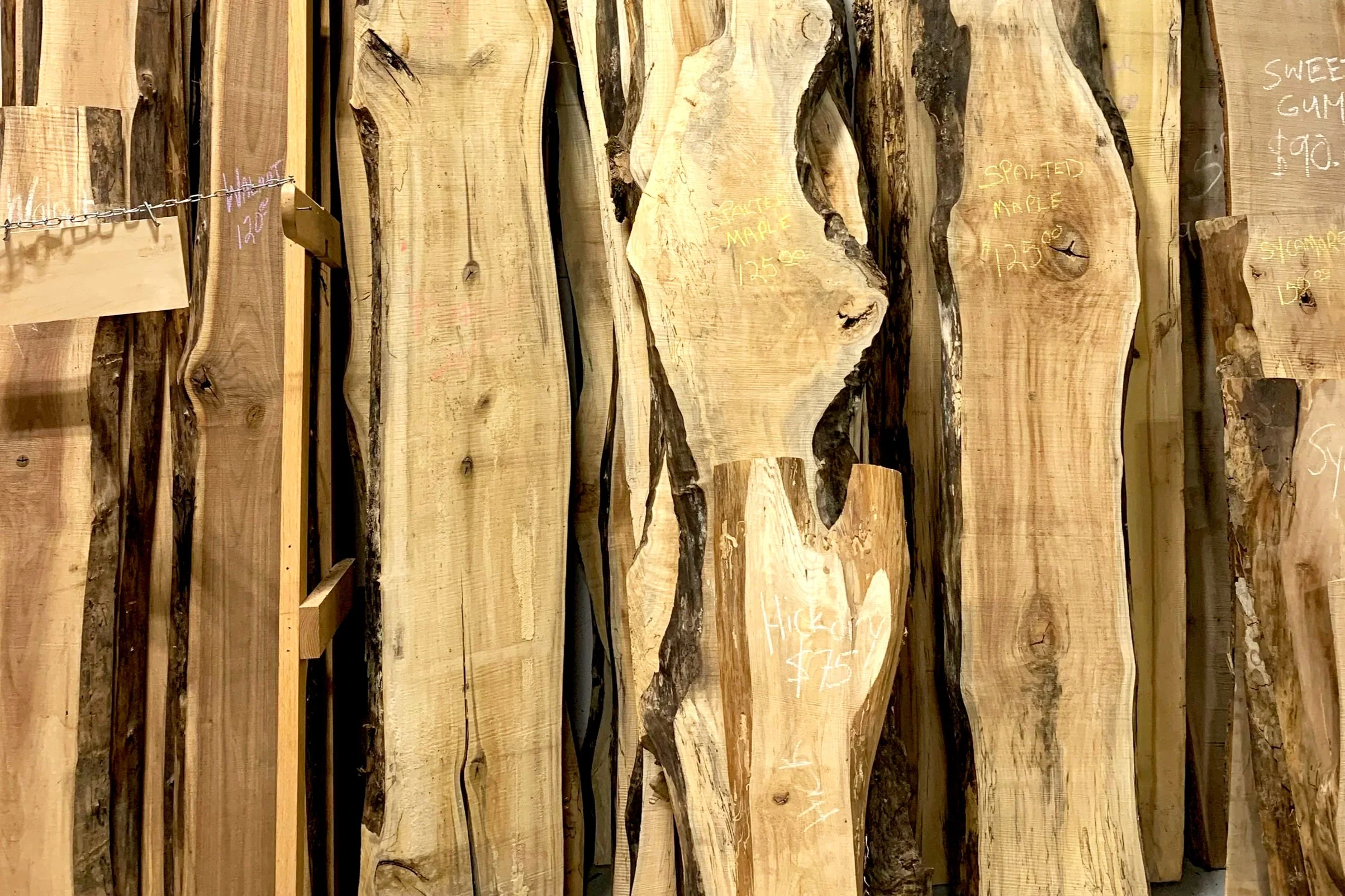 Various large slabs of wood with handwritten prices and descriptions on them, arranged vertically in a store.