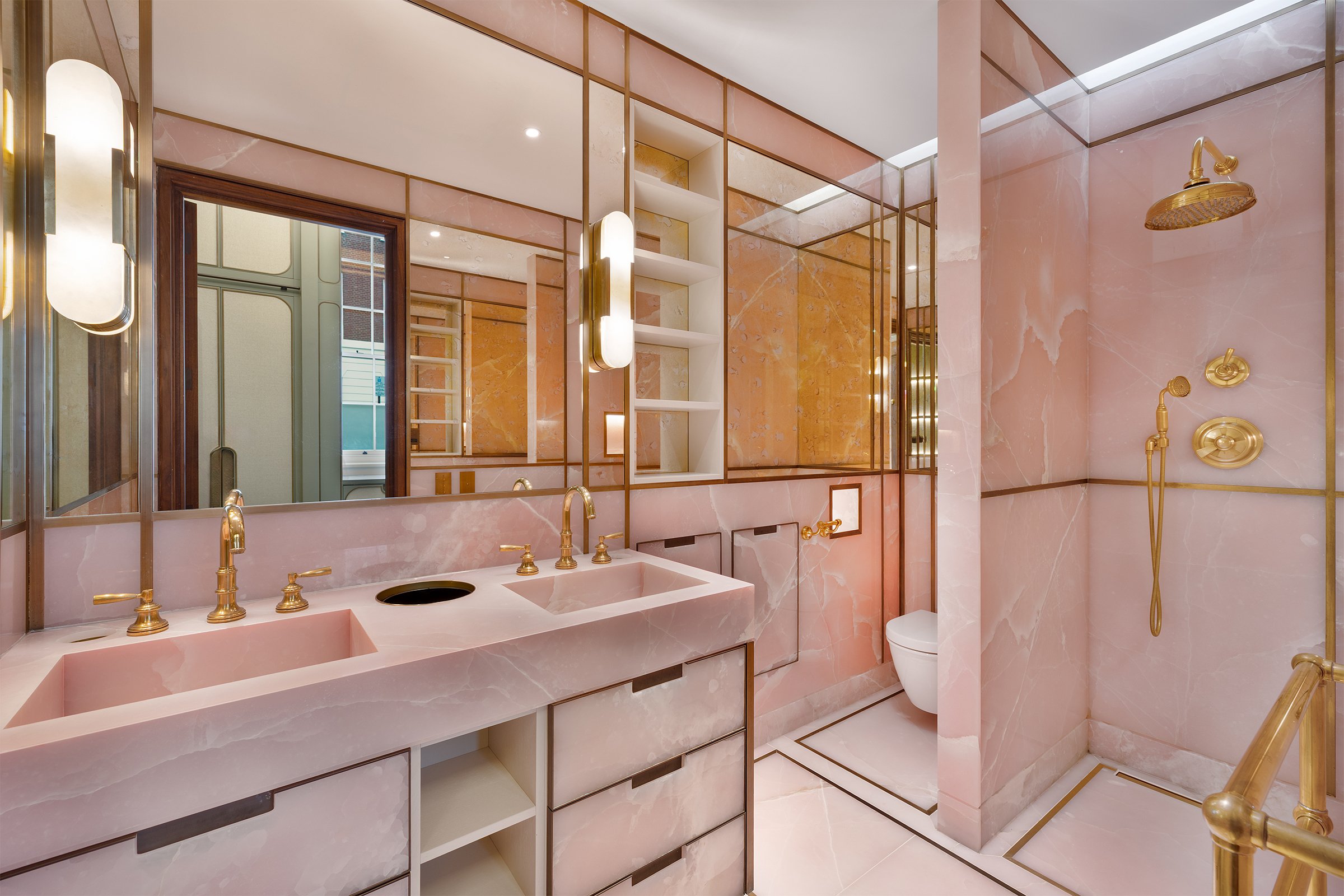 Luxurious pink marble bathroom with gold fixtures, including a double sink vanity, mirrors, and a walk-in shower with a rainfall showerhead.