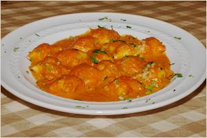 Plate of cheesy ravioli in tomato sauce garnished with parsley.