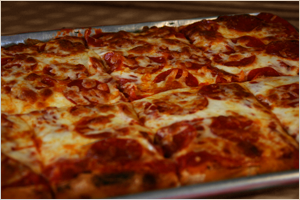 A freshly baked cheese pizza sliced into square pieces.