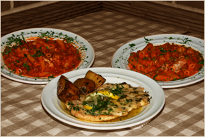 Three plates of Indian food on a wooden table, featuring two plates of curry and one plate with a bread dish.