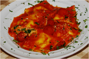 A plate of baked pasta with tomato sauce, melted cheese, cherry tomatoes, and chopped herbs.
