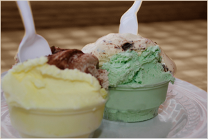 Two bowls of ice cream, one with yellow and chocolate flavors and the other with mint and chocolate flavors, each with a white plastic spoon.