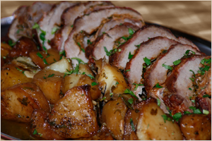 Slices of breaded meat with a brown sauce, served with roasted potatoes and garnished with chopped herbs.