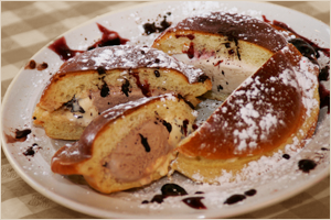 Dessert plate with sliced cannoli filled with cream and chocolate chips, dusted with powdered sugar and drizzled with chocolate sauce