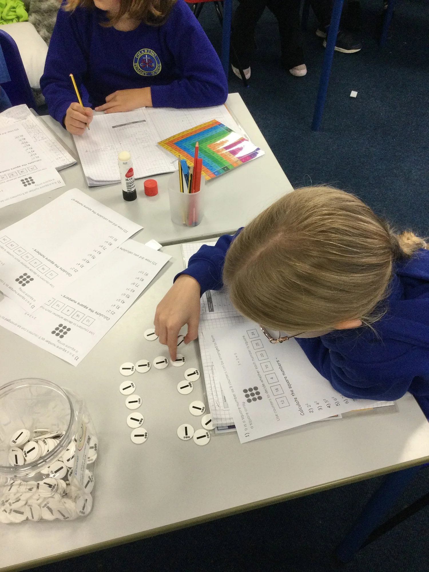 Children engaged in a math activity using counting chips and worksheets in a classroom.