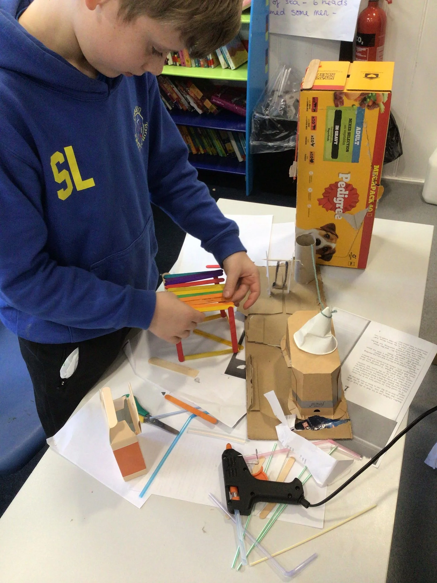 A person working on a science project with various craft materials and a glue gun on a table.