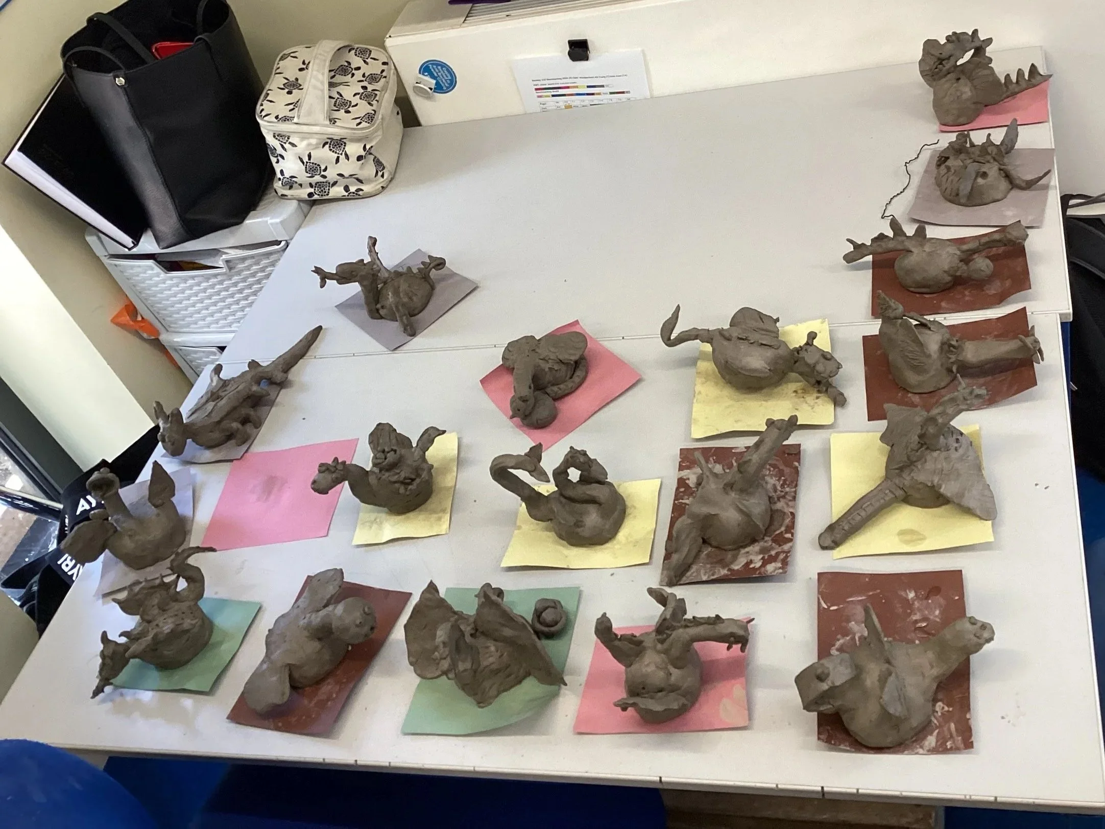 Various clay sculptures of animals and figures on a table, each placed on colorful paper squares.