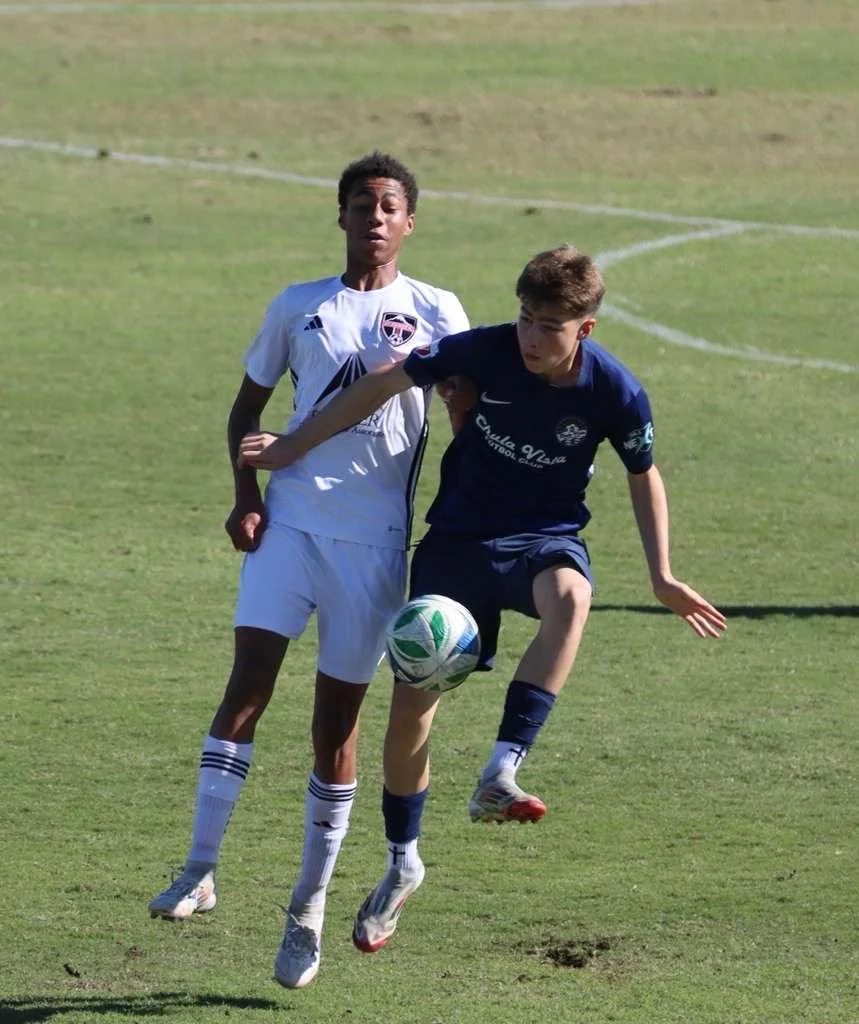 Two young soccer players competing for the ball on a grassy field during a match.